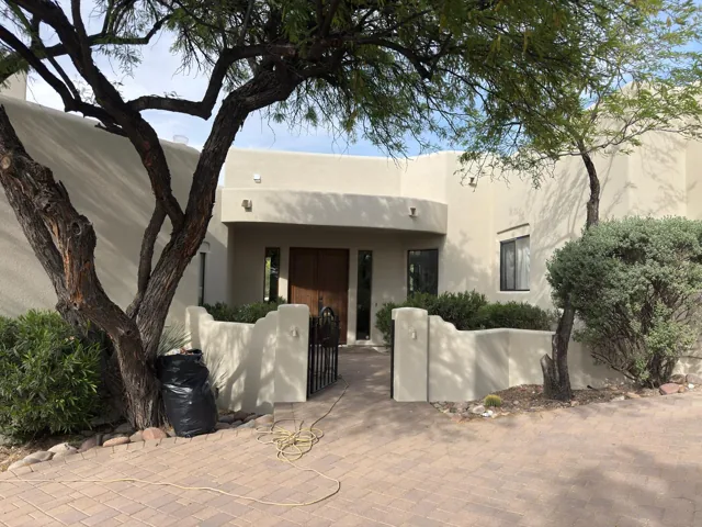 Light-colored stucco courtyard entrance framed by a mature tree
