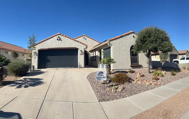 Sage-colored stucco house with a dark garage door and desert landscaping